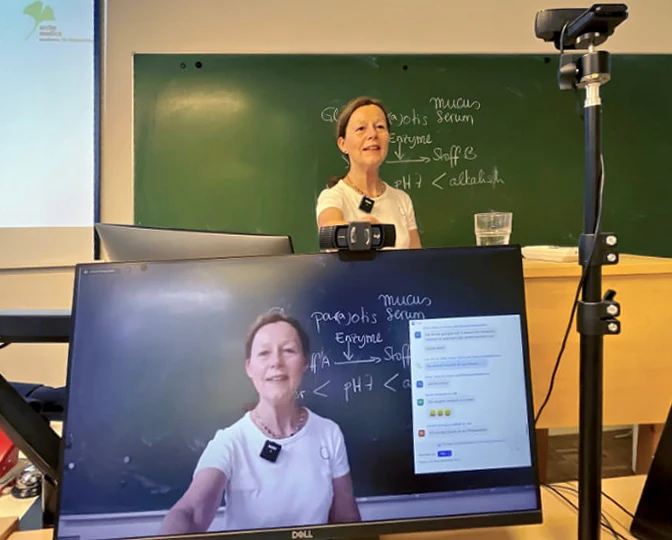 Die Dozentin im Klassenraum und zugleich groß auf dem Monitor des Livestreams
